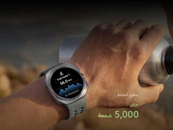 A man on a mountain trail with rocky terrain is holding a water tumbler in his hand while wearing a Galaxy Watch Ultra2 in Titanium Silver with a Marine Band in Olive, displaying a trail route with a distance, ideal for reliable guidance in challenging outdoor conditions during trail running and climbing.