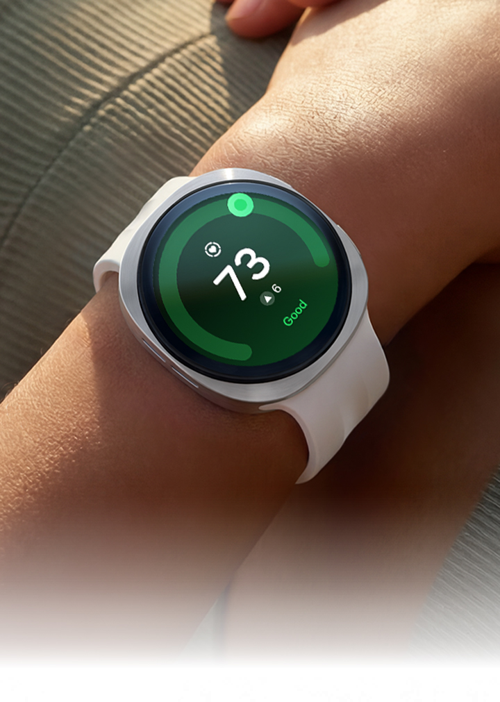 A person lying on their back is wearing Galaxy Watch9 in Cream with a Sport Band in Cream on their wrist and a Heart Health Score of 73 is shown on the watch display, showcasing the heart health tracking capabilities of Galaxy Watch9.