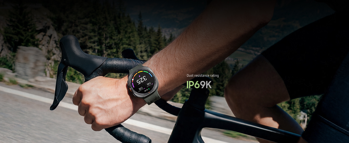 A cyclist is riding a bike on a road in the mountains while wearing a Galaxy Watch Ultra2 in Titanium Silver with a Marine Band in Olive displaying a personalized Functional Threshold Power with cadence and average power.